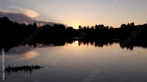 Golden sun sets behind forest silhouettes reflecting in calm lake water at dusk near Regensburg