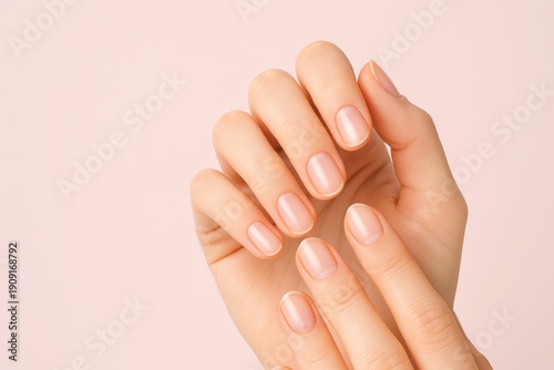 Close-up shot of a woman's hands with beautifully manicured nails, showcasing elegance and care against a soft, pastel pink background, highlighting natural beauty.