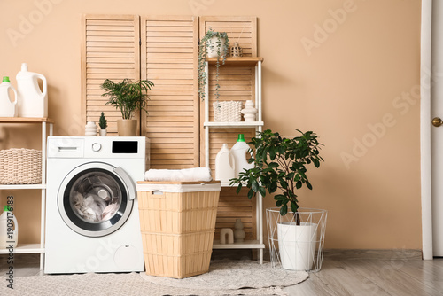 Quadro em tela Stylish laundry room with modern washing machine, basket, shelving units and bot