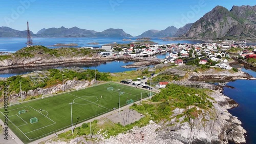 drone flight, at wonderful village Henningsvær, Henningsvaer on many small islands. Famous soccer field visible. Some people playing on the field. Wonderful touristic travel destination on Lofoten isl