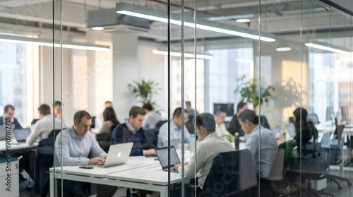 A wide view through a glass partition showcases a bright, modern open-plan office with numerous professionals intently working at their desks.