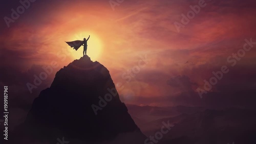 Conceptual sunset scene, superhero with cape standing brave on top of a mountain looks determined at horizon raising one hand up as a winning leader. Hero power and motivation, overcoming obstacles.