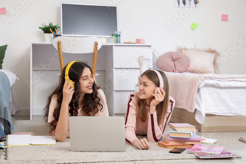Foto Female students with headphones using laptop in dorm room