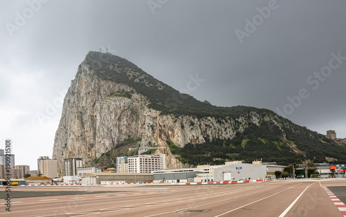 Foto View of the Rock of Gibraltar with the airport runway in the foreground and cloudy sky, showing the contrast between the urban environment and the iconic rock formation of southern Europe