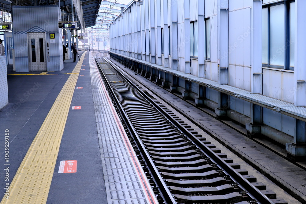 Naklejka premium 駅のホームと線路、安全を支える黄色の点字ブロックが続く風景（公共交通機関・バリアフリー）