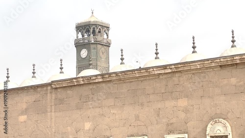 View of a historic stone wall and clock tower in Cairo, Egypt. Exterior architectural detail with traditional design elements and urban background, suitable for themes of heritage, architecture.