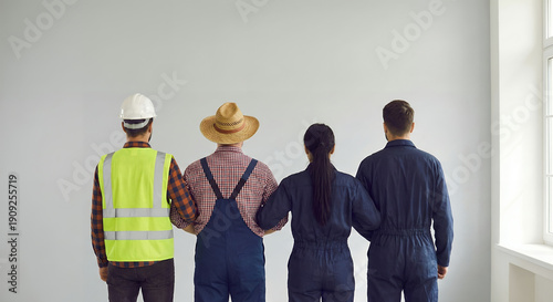 Quadro su tela Team of four workers in overalls stand together, back to camera, symbolizing col