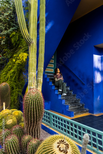 A woman sits on blue stairs surrounded by cacti. Jardin Majorelle,Marrakech,Morocco