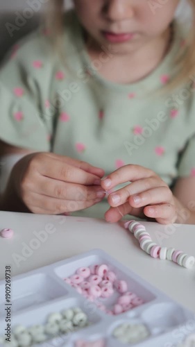 Child creating a colorful bead bracelet at a table during a sunny afternoon