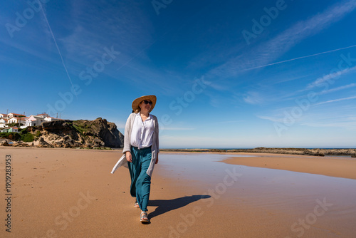 Beautiful middle-aged woman enjoying walk on sandy beach Monte Clerigo in Portugal on spring day. Front view