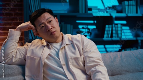 Billede på lærred Upset Asian middle-aged man choosing tv channel boring cinema at night evening i