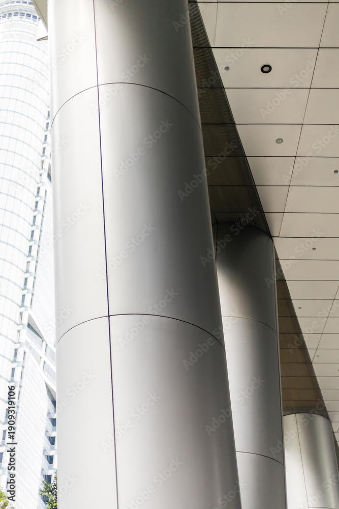 Obraz premium A set of large gray columns support the roof of a walkway in a city environment. The structure features smooth lines and contemporary materials, blending into modern architecture