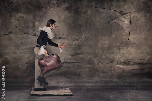 Фотография Man with long nose flying kite while holding suitcase in surreal vintage scene