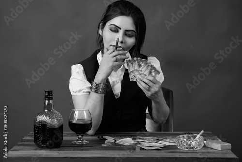 Monochrome portrait of a woman seated at a gambling table holding playing cards and smoking a cigarette, surrounded by poker chips and alcohol. Concept image illustrating high risk decisions