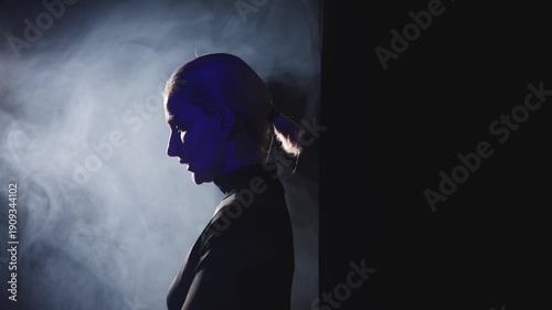 A young blonde woman with a short ponytail steps decisively into a bright side light. High-contrast video captures her profile, symbolizing the courage to speak out and overcome stage fright.