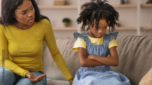 Fotografi A mother talks to her daughter who sits with arms crossed on a couch