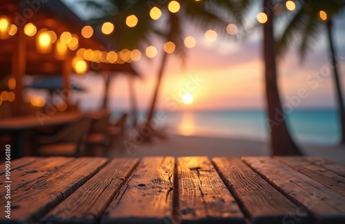 Empty wooden table with blurred beach bar and ocean sunset background. String lights glow above palm trees near tropical coast. Warm evening vacation ambience.