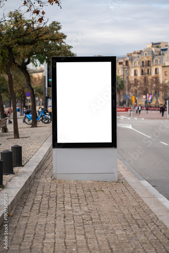 Blank vertical street billboard mockup showcasing a clean white space, ideal for advertising and marketing campaigns, positioned on a city sidewalk next to a road with blurred urban background