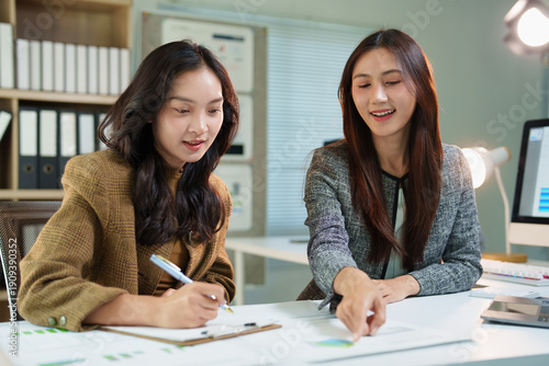Fotografie Two businesswomen discussing financial data and charts on paper in an office, wo