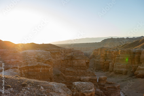 Charyn Canyon in Kazakhstan is an impressive desert landscape with towering red sandstone cliffs and a colorful sunrise that highlights the harsh beauty of nature.
