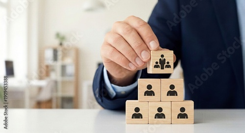Hand placing leader icon block on top of team pyramid structure for hierarchy leadership, departmental supervision and organizational command