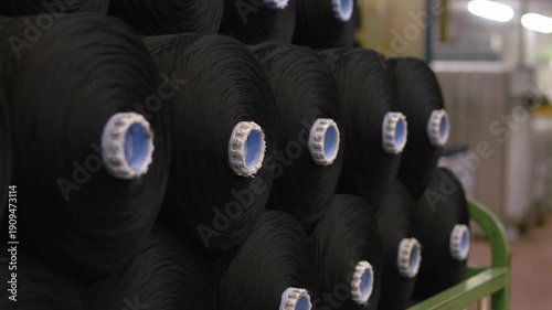 Large rolls of black fabric stacked in a textile factory warehouse. Textile materials ready for distribution and further garment manufacturing processes.