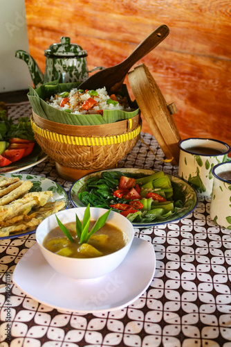 Obraz na płótnie various traditional Indonesian dishes, including rice in a bamboo basket, fried chicken, assorted vegetables, and fresh drinks