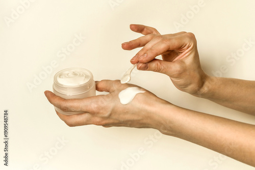 Hand, face or body cream. A woman's hand holding a mock-up of a white glass jar with cream on a light background. The concept of cosmetics, skin care, nutrition and hydration.