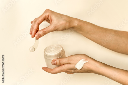 Hand, face or body cream. A woman's hand holding a mock-up of a white glass jar with cream on a light background. The concept of cosmetics, skin care, nutrition and hydration.