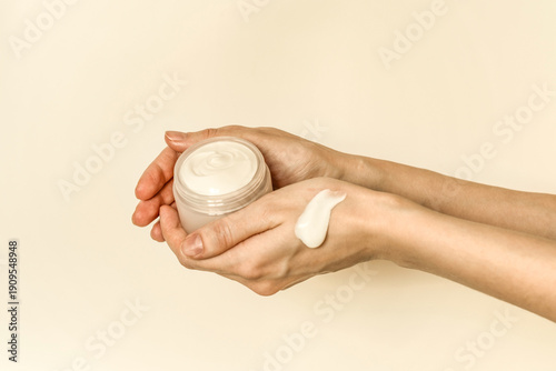 Hand, face or body cream. A woman's hand holding a mock-up of a white glass jar with cream on a light background. The concept of cosmetics, skin care, nutrition and hydration.