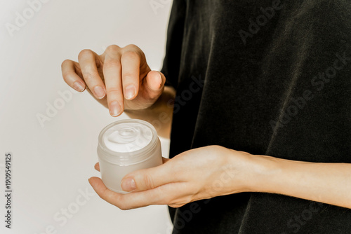 Hand, face or body cream. A woman's hand holding a mock-up of a white glass jar with cream on a light background. The concept of cosmetics, skin care, nutrition and hydration.