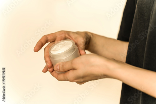 Hand, face or body cream. A woman's hand holding a mock-up of a white glass jar with cream on a light background. The concept of cosmetics, skin care, nutrition and hydration.
