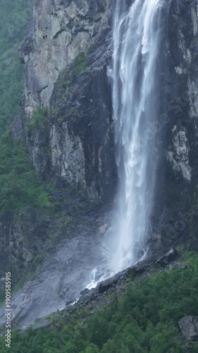 backward drone flight, View on big waterfall in Romsdalen valley, falling from a high cliff, during rainy day in summer. Steep mountain cliffs, rocks, pristine forest. Amazing wilderniss in Norway. Re