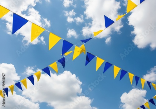 Bright yellow and blue triangular pennant flags strung across a vibrant blue sky filled with fluffy white clouds, creating a festive and celebratory atmosphere