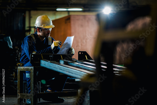 Industrial worker measuring a metal component in a factory workshop while wearing safety helmet and gloves, ensuring precision, quality control, and workplace safety in manufacturing process.