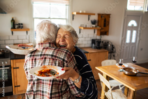 Senior couple hugging and laughing in cozy home kitchen after lunch
