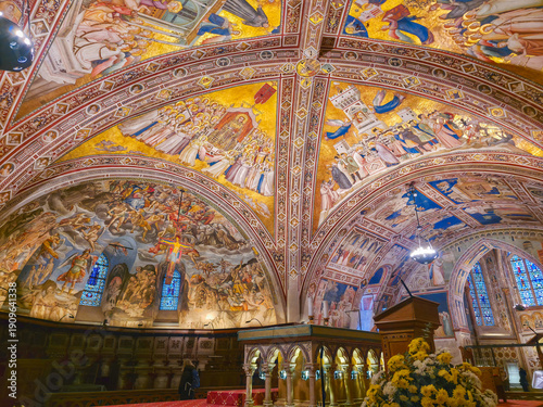 Interior view of the Lower Basilica of San Francesco in Assisi, Italy, featuring ornate frescoed vaults, medieval art masterpieces, and the high altar in a spiritual atmosphere
