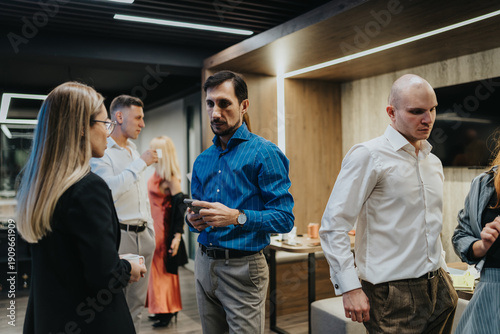 Photos A diverse group of coworkers mingle in a contemporary office setting, some holding cups and chatting