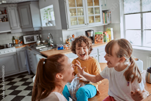 Obraz na plátne Mother and two children laughing together in home kitchen