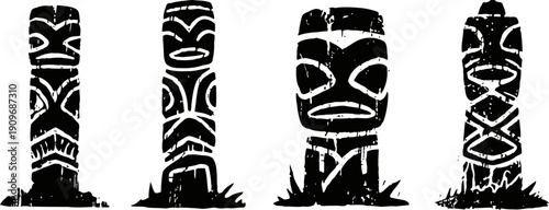 Set of four black and white tiki totem statues with grass at the base in traditional polynesian tribal