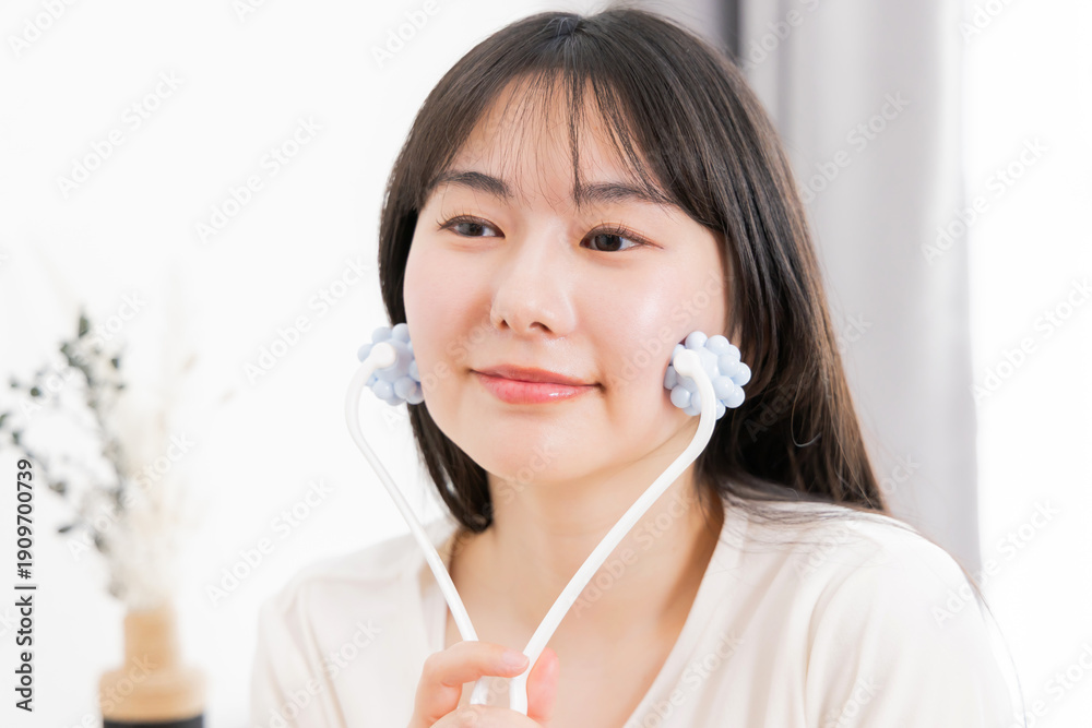 Naklejka premium 美顔器でマッサージするパジャマ姿の若いアジア人女性 