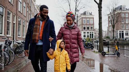 Family of three walking on a wet cobblestone street with bicycles
