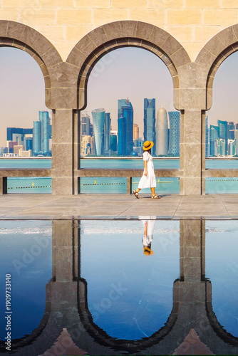 Woman tourist walking near Museum Islamic Art Doha with stone arches framing modern skyline reflected in water Middle East travel lifestyle architecture landmark
