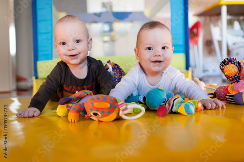 Quadro em tela Two cheerful infants play together on a vibrant yellow mat, surrounded by an array of colorful toys