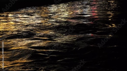 The sea rippling in the reflection of the city lights at night. Background video: Sea waves against a dark and emotional atmosphere.