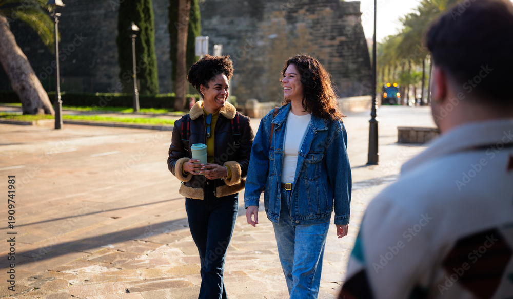 Fototapeta premium Two friends strolling a sunny city street, laughing and chatting over coffee, casually dressed and enjoying a relaxed urban weekend together in warm daylight and autumn breezes