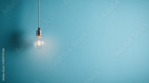 A glowing light bulb suspended from a cord against a blue wall viewed from a slight angle