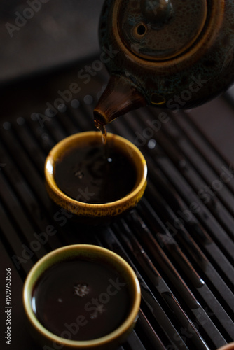 Pouring Tea from Teapot into Small Cup on Tea Table Close Up