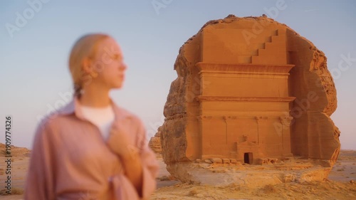 Woman tourist travels to Saudi Arabia, visits Hegra in AlUla, looking at tombs at sunset