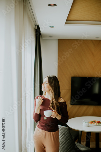 Woman stands by window hold...
